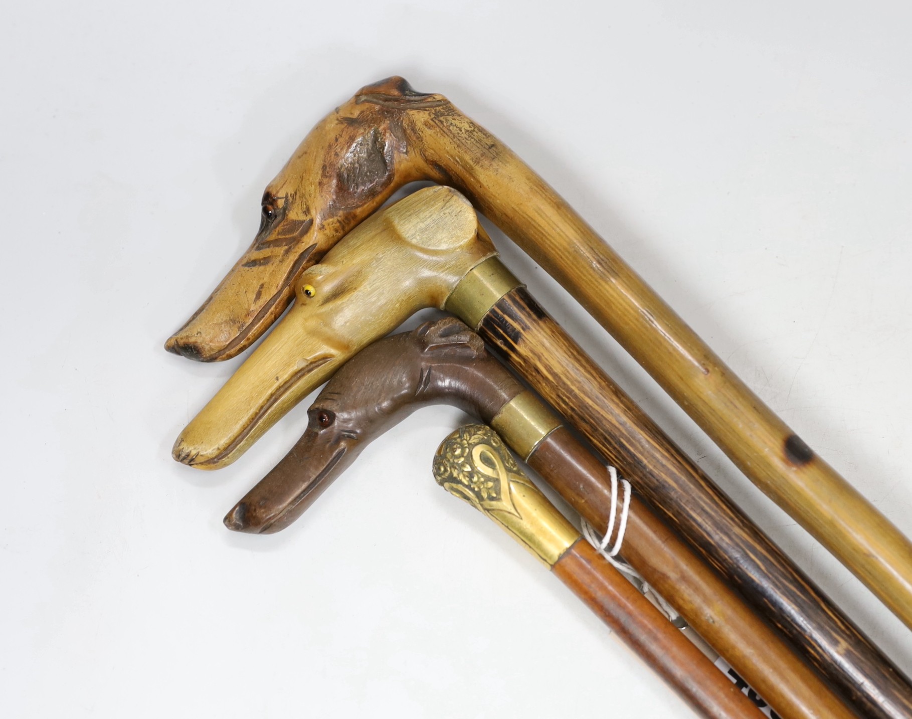 Four walking sticks: The first with carved horn dog‘s head handle, two with carved wood dogs head handles, one gilt metal mounted handle, tallest 86cms